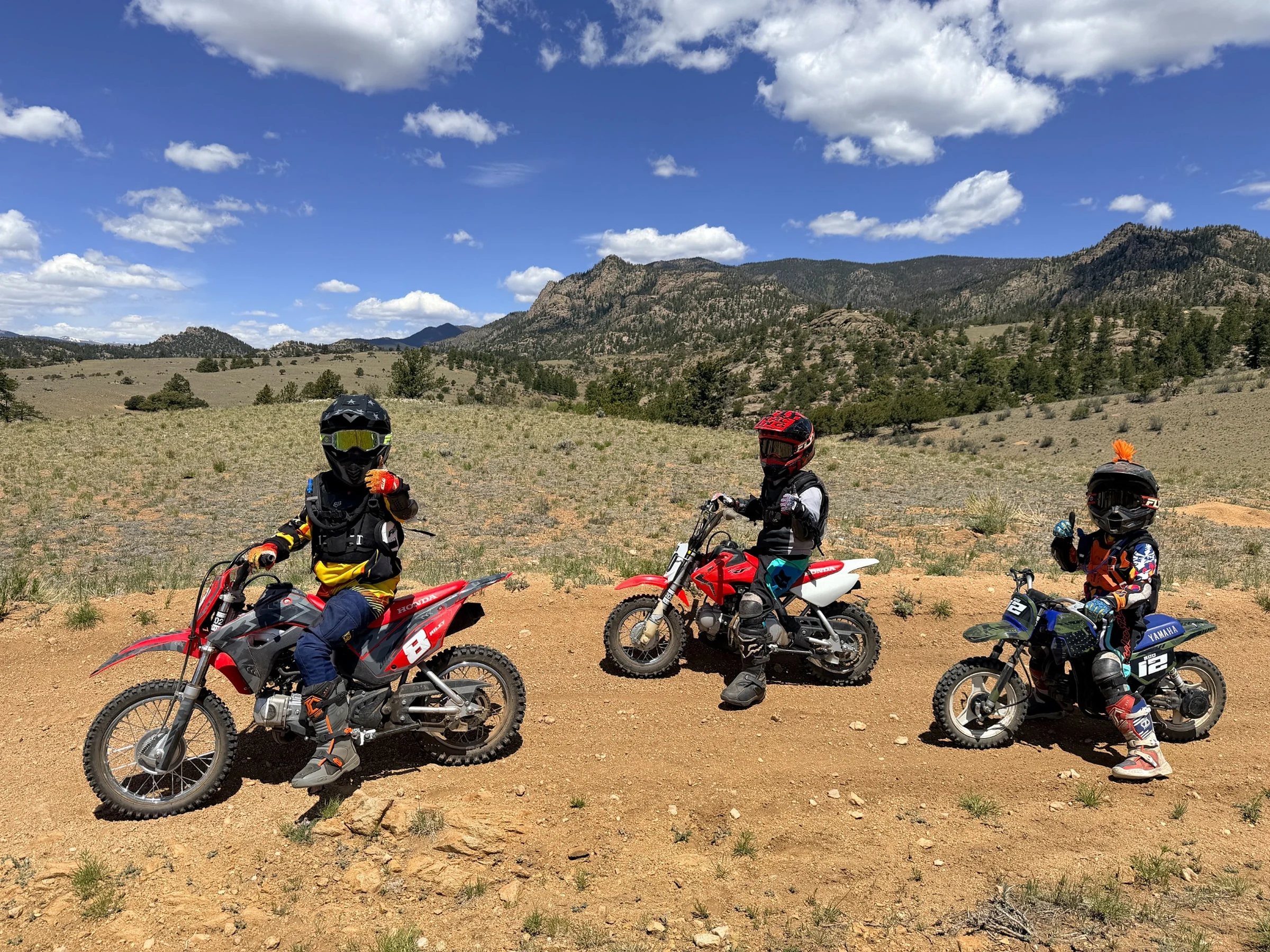 Three boys on dirt bikes with mountains behind them