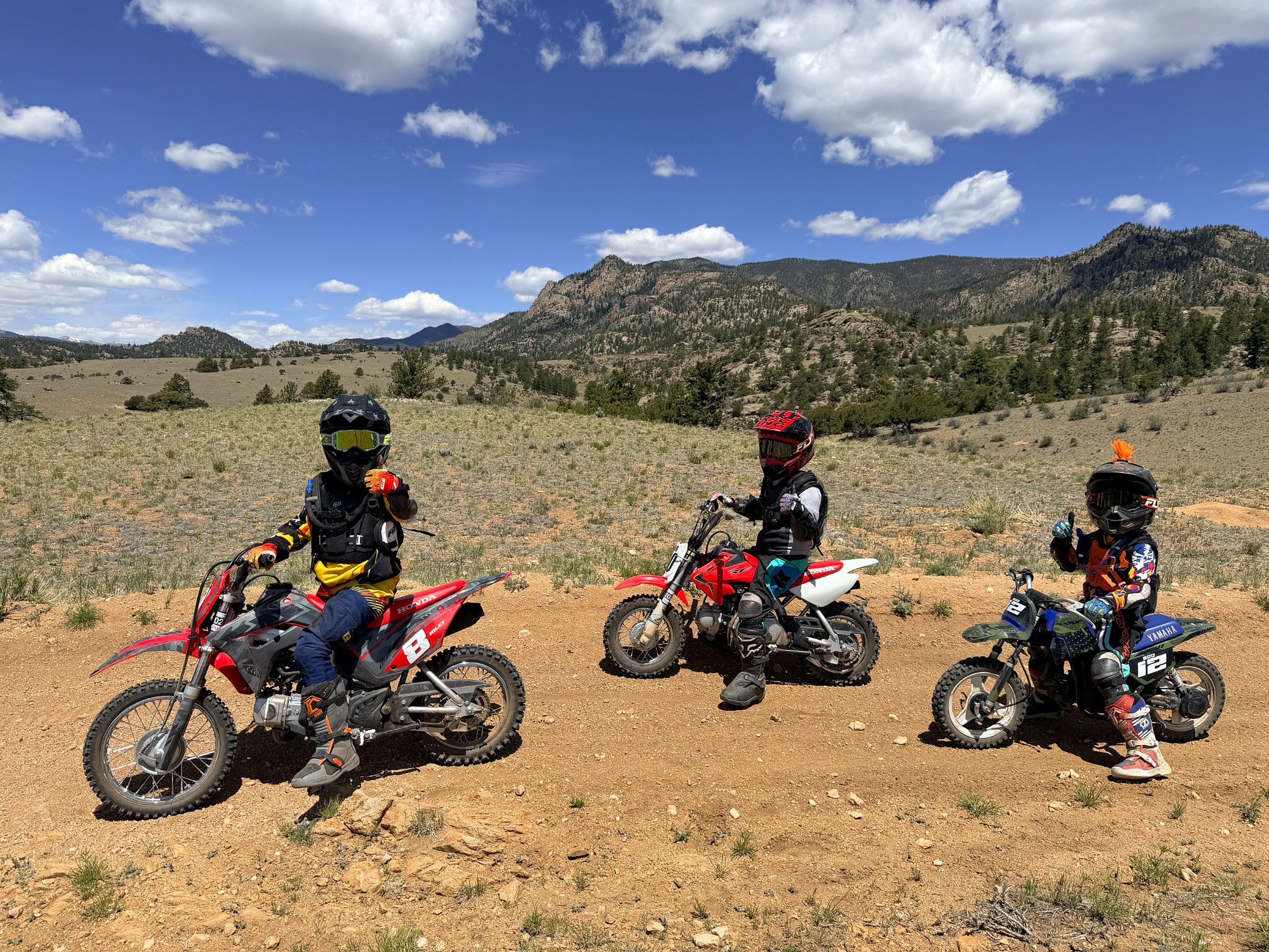 Three boys on dirt bikes with mountains behind them